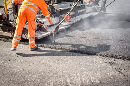 Neubau einer Straße, Walze glättet Asphalt, Arbeiter überprüft Belag. 