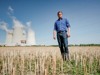 Landesrat Stefan Kaineder auf einem Feld, im Hintergrund Kühltürme und Betriebsgebäude des Atomkraftwerkes Temelin