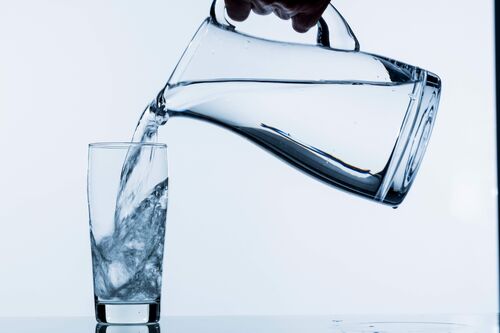 Wasser wird aus Krug ins Glas geschenkt 