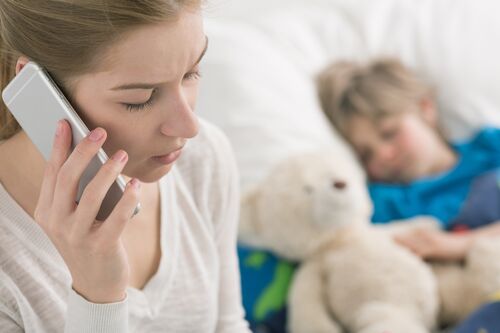 Eine Mutter sitzt am Bett ihres kranken Kindes und telefoniert mit einem Handy