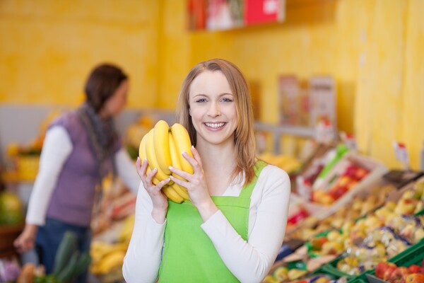 Lehrling mit Obst in Händen vor einem Obstregal im Supermarkt