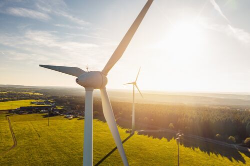 Nahaufnahme von zwei Windrädern, Landschaft mit Feldern, Betriebsgebäuden und Wäldern