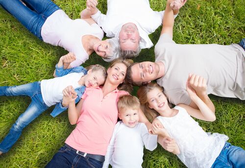 Drei Generationen einer Familie, sieben Menschen, liegen im Kreis mit den Köpfen zueinander auf einer Wiese