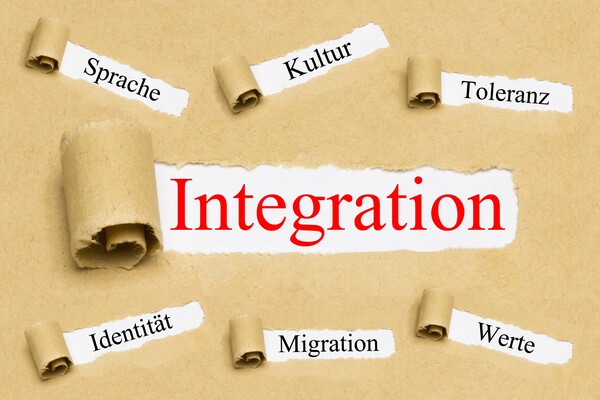 Papier rollt sich auf und gibt Worte wie Sprache, Kultur, Toleranz und Werte frei, mittig das Wort Integration