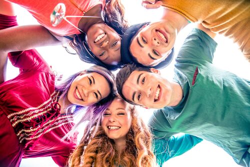 Fünf fröhliche Jugendliche stehen im Kreis mit den Köpfen zueinander