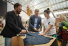 WeFair-Geschäftsführer Wolfgang Pfoser-Almer, LR Stefan Kaineder und eine Frau auf der WeFair 2021 in Linz. Sie bearbeiten ein T-Shirt mit Schere und Filzschreiber.