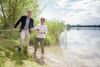 Landesrat Stefan Kaineder und Ing.in Sabine Kapfer stehen nebeneinander an einem Seeufer, beide halten eine Wasserprobe, die sich in einem Kunststoffgefäß an einer langen Stange befindet
