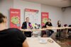 KLandesrat Stefan Kaineder, Wolfgang Pfoser-Almer und Miriam Bahn an einem Konferenztisch mit Mikrofonen, im Hintergrund drei Plakate der WearFair-Messe, im Vordergrund ein Journalist 