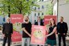 Konrad Rehling, Wolfgang Pfoser-Almer, Landesrat Stefan Kaineder, Miriam Bahn und Norbert Rainer stehen in einer lockeren Gruppe und zeigen ein Plakat der WearFair-Messe, im Hintergrund Bäume und das Gebäude des Ursulinenhofes