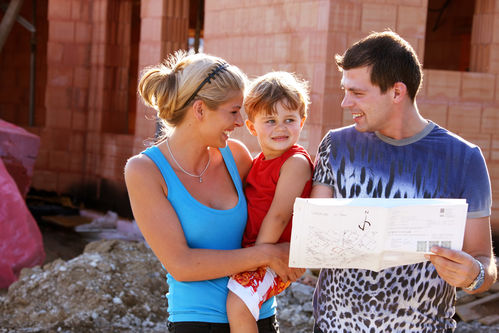 Eltern mit Kind und Plan vor einer Hausbaustelle