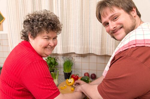 Mann und Frau mit Beeinträchtigungen beim Schneiden von Paprika 