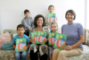 Landesrätin Birgit Gerstorfer und Jasmine Chansri sitzen nebeneinander auf einem Sofa, mit ihnen vier Kinder, fast alle halten jeweils das Buch „Das kleine Ich bin ich“ in Händen