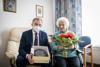 Landeshauptmann Mag. Thomas Stelzer mit einer Geburtstagstorte und Stefanie Kürner mit einem Blumenstrauß in ihrem Zimmer.