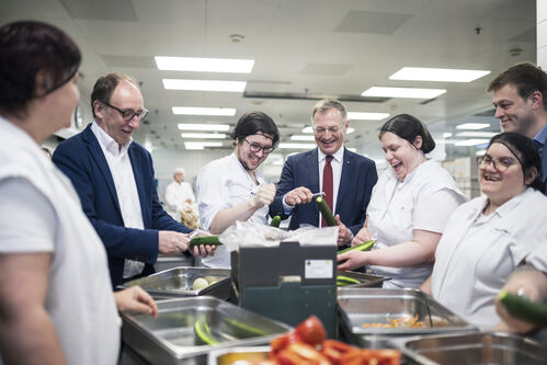 Sozial- und Gesundheitsminister Johannes Rauch, Landeshauptmann Thomas Stelzer und Landesrat Stefan Kaineder beim Gurkenschälen mit dem engagierten Küchenteam der Betriebsküche im Landesdienstleistungszentrum.