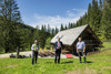 Landesrat Max Hiegelsberger, Landeshauptmann Mag. Thomas Stelzer und Helmut Immitzer auf einer Wiese vor einer Almhütte mit Sitzgelegenheiten und einem Brunnen aus Holz, dahinter ein Wald