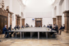 Circa zwanzig Personen, alle mit FFP2-Maske, sitzen rund um einen sehr großen Tisch im Steinernen Saal des Linzer Landhauses