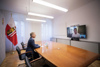 Landeshauptmann Stelzer in einer Videokonferenz mit Bundeskanzler Karl Nehammer, der Landeshauptmann sitzt an einem langen Tisch in einem Büro, im Hintergrund Oberösterreich-Flagge, gegenüber der Videoscreen mit dem Bundeskanzler in Halbtotale. 