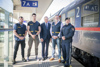 Daniel Moser, Dennis Moro, Landeshauptmann Mag. Thomas Stelzer, Gerhard Kugelgruber (Dienststellenleiter der PI Linz Hauptbahnhof) und Dominik Bründl stehen nebeneinander auf einem Bahnsteig; rechts von ihnen steht ein Zug. 