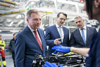 Landeshauptmann Mag. Thomas Stelzer, Milan Nedeljković (Produktionsvorstand der BMW AG) und Bundeskanzler Karl Nehammer stehen nebeneinander in einer Fertigungsstraße; vor ihnen ist ein Motor, der von einer Mitarbeiterin erklärt wird, zu sehen.  