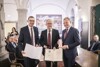 v.l.: Bürgermeister Ing. Markus Vogl, Bgm. a.D. Konsulent Gerald Hackl und Landeshauptmann Mag. Thomas Stelzer stehen nebeneinander in einem Saal; Markus Vogl und Gerald Hackl halten je eine Urkunde, Landeshauptmann Stelzer das Goldene Ehrenzeichen für die Verdienste um die Republik Österreich in Händen