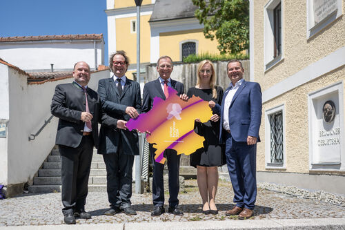 St. Florians Bürgermeister Bernd Schützeneder, der künstlerische Leiter des Bruckner-Jahrs 2024 Norbert Trawöger, Landeshauptmann Thomas Stelzer, Kulturdirektorin Margot Nazzal und Ansfeldens Bürgermeister Christian Partoll mit dem Logo des Bruckner-Jahrs 2024 in Form einer Oberösterreich-Karte vor dem Geburtshaus von Anton Bruckner in Ansfelden.