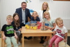 Landeshauptmann-Stellvertreterin Mag.a Christine Haberlander und Landesrat Markus Achleitner stehen in einem Raum, vor ihnen ein kleiner Tisch, an dem fünf Kinder verschiedenen Alters spielen