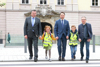 Landesrat Mag. Günther Steinkellner, Landeshauptmann-Stellvertreter Dr. Manfred Haimbuchner und Landesrat Ing. Wolfgang Klinger stehen mit zwei Schulkindern zwischen ihnen händehaltend nebeneinander, die Kinder tragen Warnwesten, im Hintergrund das Südportal des Linzer Landhauses