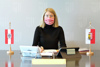 LH-Stellvertreterin Mag.a Christine Haberlander mit Mund-Nasen-Schutz an einem Bürotisch auf dem kleine Oberösterreich-Fahnen aufgestellt sind