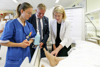 LH-Stv.in Mag.a Christine Haberlander und Geschäftsführer der OÖG Mag. Karl Lehner stehen mit einer Schülerin vor einem Krankenhausbett, Haberlander berührt den Fuß einer Krankenpflegepuppe, die im Bett liegt. 
