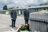 Landeshauptmann Mag. Thomas Stelzer und Bundespräsident Dr. Alexander Van der Bellen stehen mit gesenktem Kopf vor einem Denkmal, vor dem ein großer Kranz liegt, im Hintergrund Baracken-Gebäude