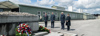 Robert Eiter, Landeshauptmann Mag. Thomas Stelzer, Bundespräsident Dr. Alexander Van der Bellen und Mag.a Doris Schmidauer stehen vor einem Denkmal, vor dem ein großer Kranz liegt, im Hintergrund Baracken-Gebäude und gedenken der Opfer des Nationalsozialismus