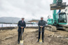 Landeshauptmann Dr. Wilfried Haslauer und Landeshauptmann Mag. Thomas Stelzer, beide mit Schutzhelm und Spaten, auf einer Baustelle, im Hintergrund ein Bagger und ein Haus mit Beschriftung Schafbergbahn