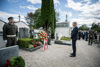 Landeshauptmann Thomas Stelzer steht auf einem Friedhof vor einem mit einem Blumenkranz geschmückten Grab, das von drei Soldaten flankiert wird