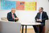 Bundespräsident Dr. Alexander Van der Bellen und Landeshauptmann Mag. Thomas Stelzer beim Gespräch sitzend an einem kleinen Tisch, im Hintergrund an der Wand ein modernes Gemälde
