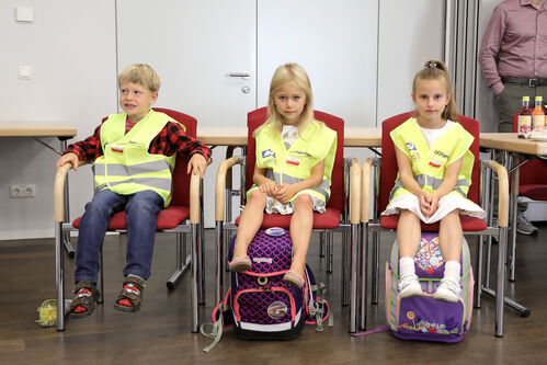 Drei Kinder sitzen mit Sicherheitswesten und Schultüten neben einander 