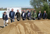 Acht Personen stehen nebeneinander hinter einem großen Sandhaufen, alle halten jeweils einen mit Sand beladenen Spaten in Händen