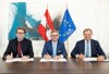 Die Bundesminister Martin Polaschek, Magnus Brunner sitzen mit LH Thomas Stelzer nebeneinander an einem Tisch. Dahinter hängt eine EU- und eine Österreich-Fahne die politische Grundsatzvereinbarung. Ein modernes Bild hängt an der Wand.