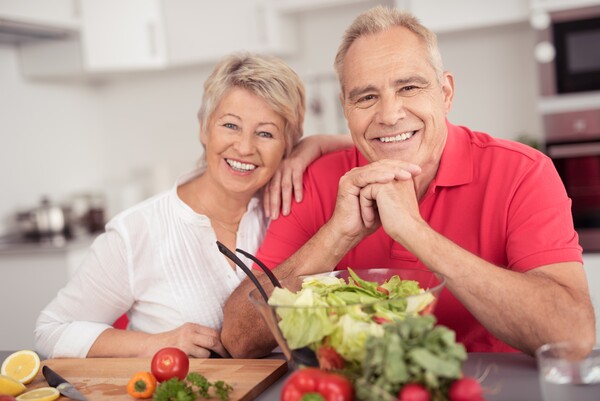 Älteres Ehepaar sitzt nebeneinander, die beiden haben eine Schüssel mit Salat vor sich. 