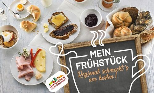 Sujet mit der Aufschrift: Mein Frühstück - Regional schmeckt’s am besten! und verschiedenen Produkten wie Käse, Schinken, Ei, Marmelade, Honig, Müsli und Gebäck im Hintergrund