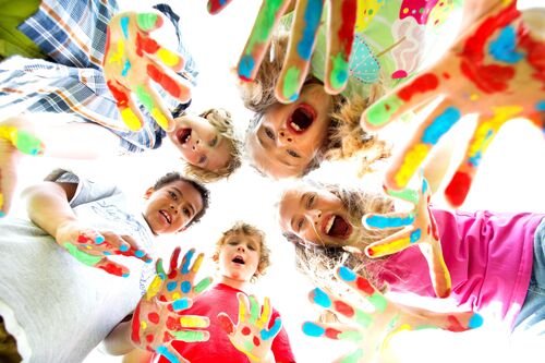 Lachende Kinder mit bunt bemalten Händen stehen im Kreis