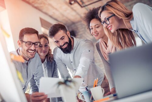 Junge Frauen und Männer gemeinsam am Arbeitsplatz, im Vordergrund ein Notebook