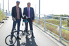 zwei Männer stehen mit Rad auf einem asphaltierten Weg