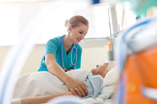Krankenschwester an einem Spitalsbett, in dem eine ältere Patientin liegt