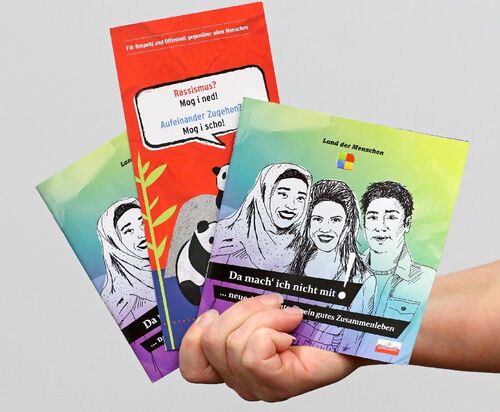 Hand hält drei Broschüren zum Thema Antirassismus und Fremdenfeindlichkeit