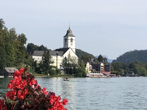 St. Wolfgang mit See und Blumen im Vordergrund und einem Beherbergungsbetrieb im Hintergrund