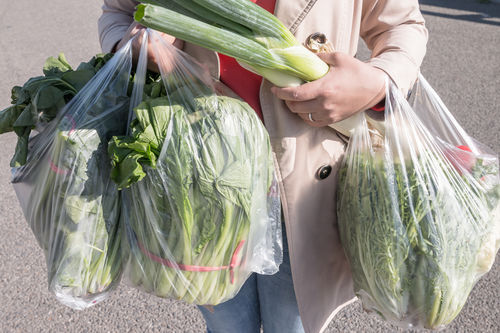 Frau trägt Salate in Plastiksackerln