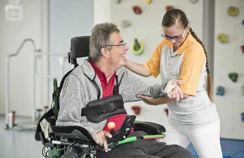 Therapeutin hebt Arm von Mann im Elektro-Rollstuhl