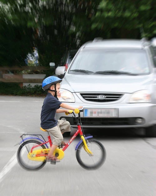 Kind fährt mit Rad bei Auto vorbei