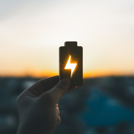 Hand hält ein Batteriesymbol gegen die Sonne.