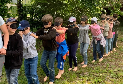 Kinder gehen mit verbundenen Augen barfuß über eine Wiese.